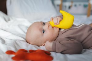 niemowlę wkładające do buzi żółty gryzak dla dzieci