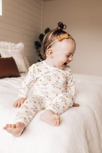 dziewczynka ubrana w biały pajac niemowlęcy siedzi na łóżku
